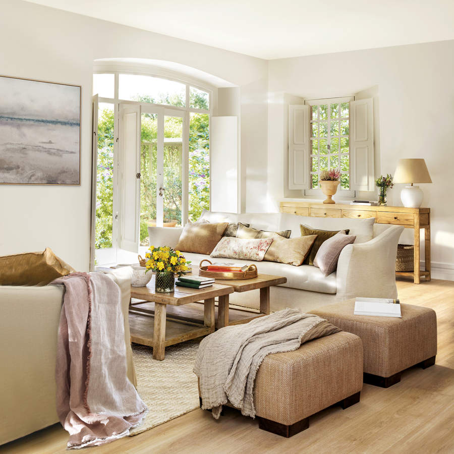 salón con sofás blancos y puf tapizado beige, alfombra blanca y suelo de parquet, flores amarillas